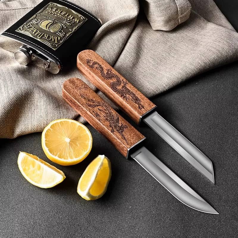 Deux couteaux japonais Tanto à manches en bois gravés dragon avec lames apparentes, posés sur un tissu beige à côté d'un citron coupé et d'une flasque noire.