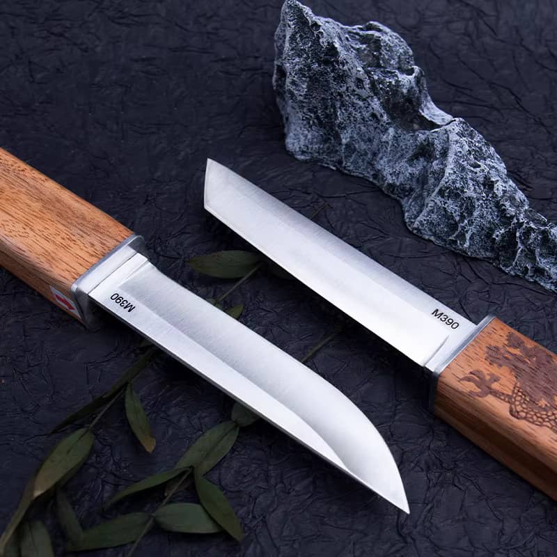 Gros plan sur les lames robustes en acier M390 de deux couteaux japonais Tanto à double lame, manches en bois gravés dragon, sur un fond texturé sombre avec décoration minérale.