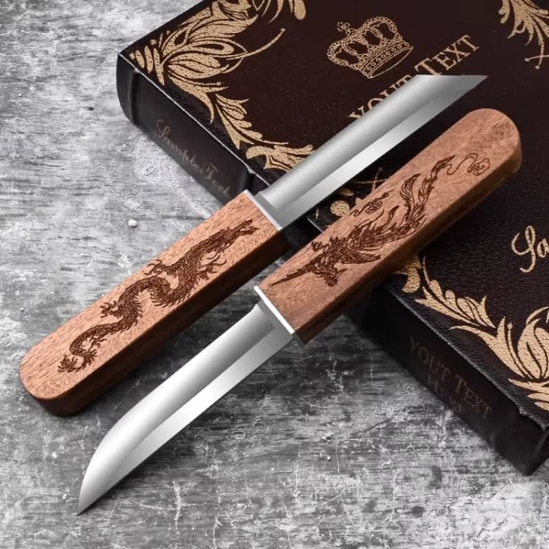 Présentation élégante de deux couteaux japonais Tanto aux manches gravés dragon et phénix, posés sur leur coffret décoratif noir sur fond gris texturé.