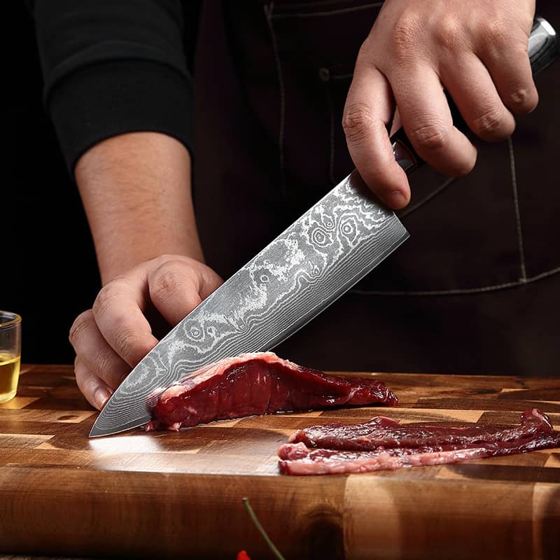 Un cuisinier qui découpe une viande avec un couteau de cuisine japonais en acier damas