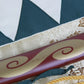 Détail du motif spirale doré peint sur le fourreau rouge du katana Mugen, élément emblématique de la série Samurai Champloo.