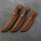 Trois étuis en cuir Punisher marron vus de dos, couture orange, avec passant ceinture, posés sur un fond béton gris texturé.
