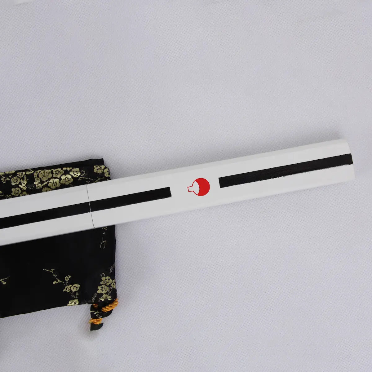 Gros plan sur le fourreau blanc du katana Sasuke Uchiwa Kusanagi de Naruto, décoré de l’emblème rouge du clan Uchiwa et d’une ligne noire, posé sur une housse en soie noire à motifs dorés, réplique en acier carbone 1045 haut de gamme idéale pour collection et cosplay.