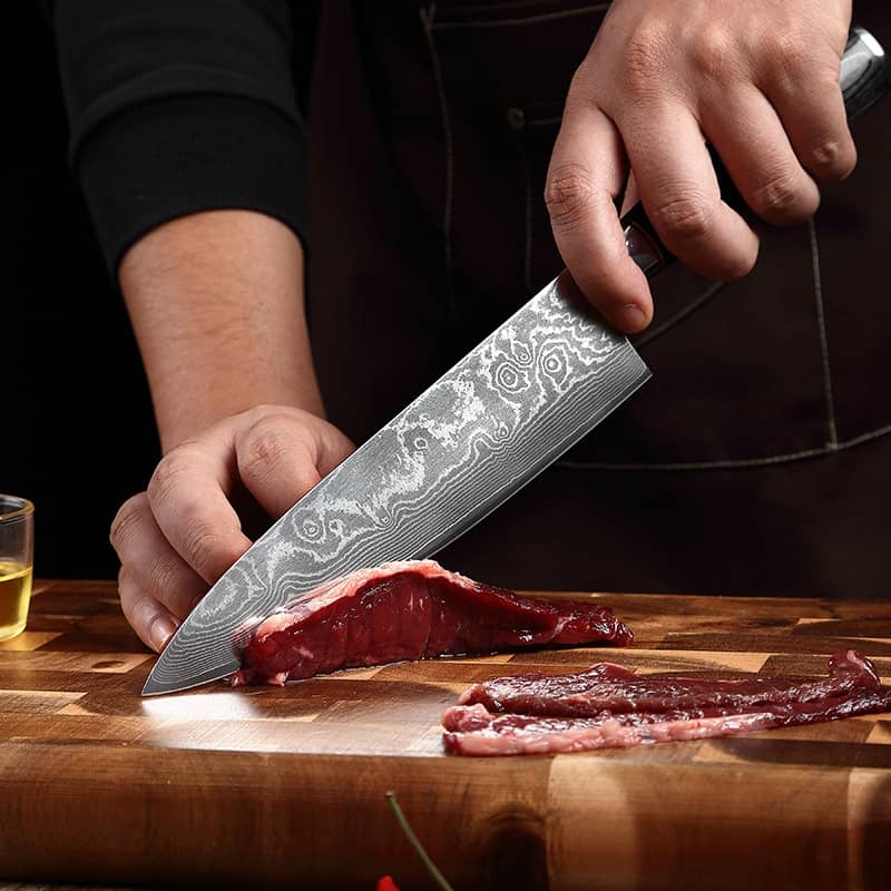 Un cuisinier qui découpe une viande avec un couteau de cuisine japonais en acier damas 